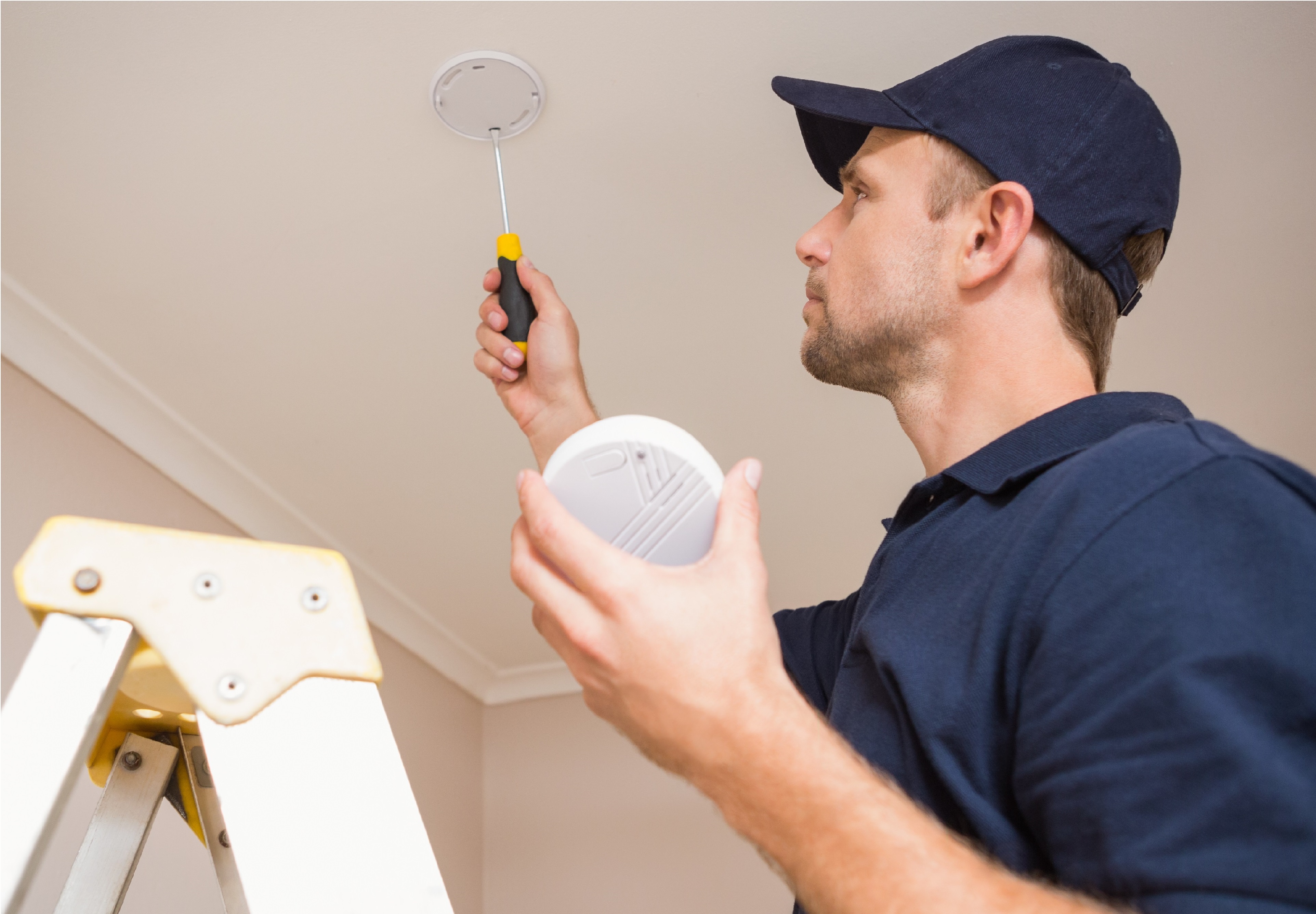 Handyman installing smoke detector with screwdriver on the ceiling